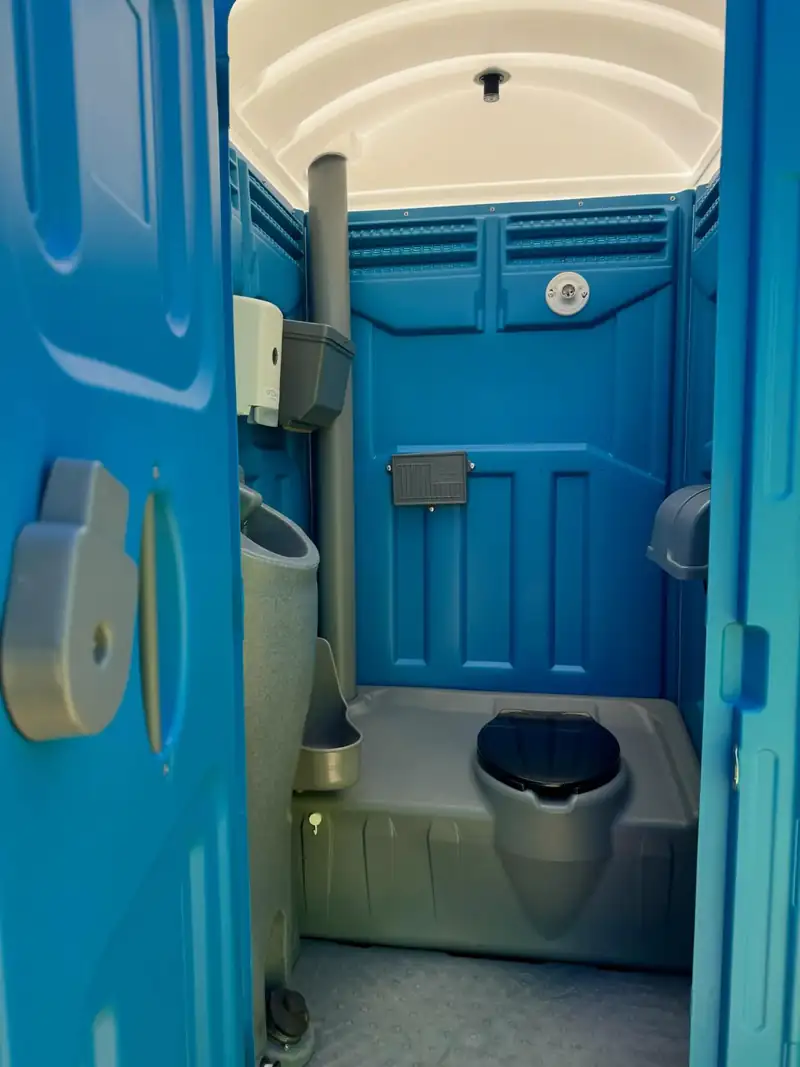 Inside a serviced standard porta potty in Midland, TX: seat, urinal and stocked toilet paper